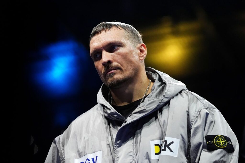 Oleksandr Usyk holding his unified heavyweight championship belts aloft in the boxing ring