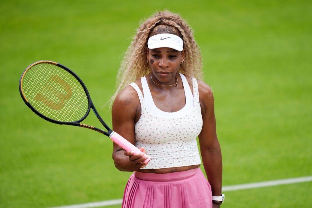 Serena Williams dressed in traditional white hitting a tennis ball on a grass practice court at Wimbledon