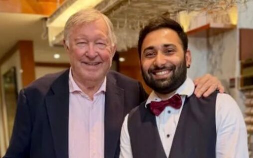 Sir Alex Ferguson smiling warmly alongside a supporter in a restaurant following his recent recovery